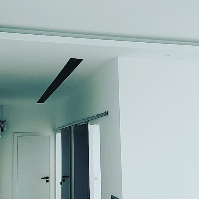 Minimalistyczne wnętrze: białe ściany, sufit z wpuszczonym elementem oświetleniowym oraz przesuwne drzwi na metalowej szynie.