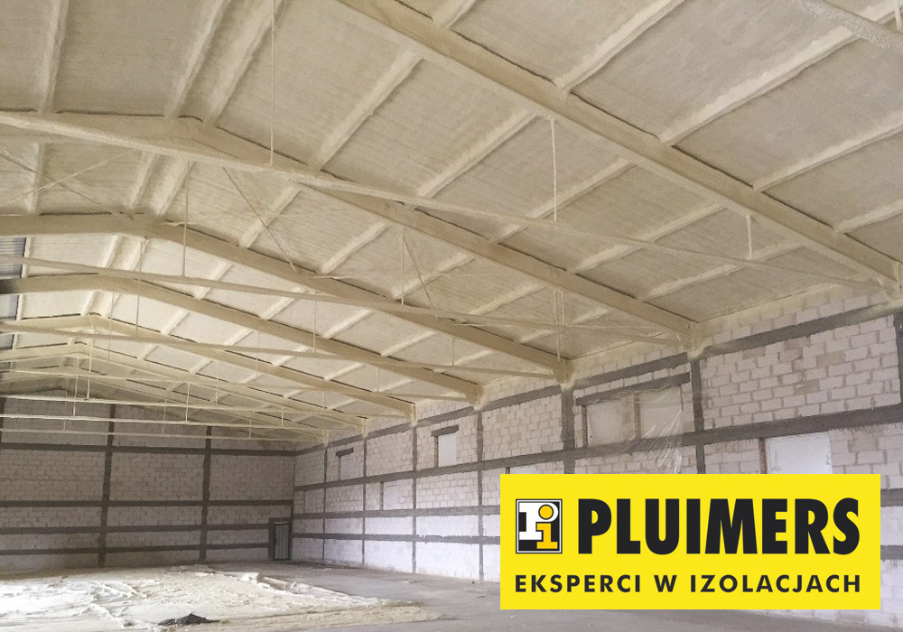 Wnętrze hali magazynowej z ocieplonym pianką PUR dachem i ścianami z bloczków, widoczne białe belki konstrukcyjne i logo firmy Pluimers w prawym dolnym rogu.