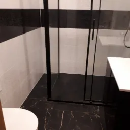 Nowoczesna łazienka w czarno-białej kolorystyce z kabiną prysznicową typu walk-in, umywalką nablatową i podłogą z czarnego marmuru z białymi żyłkami.