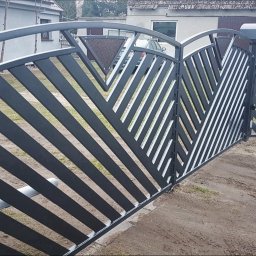 MarkoSpaw - Nowoczesna, czarna brama wjazdowa z ukośnymi, białymi przerwami, wyposażona w automat, z widocznym numerem domu w tle.