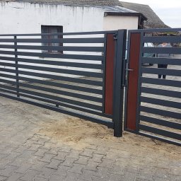 MarkoSpaw - Nowoczesna brama wjazdowa przesuwna z poziomymi panelami w kolorze grafitowym i brązowymi akcentami, widoczna na tle kostki brukowej i budynku z numerem 4.