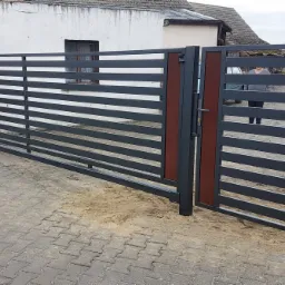 Nowoczesna brama wjazdowa przesuwna z poziomymi panelami w kolorze grafitowym i brązowymi akcentami, widoczna na tle kostki brukowej i budynku z numerem 4.