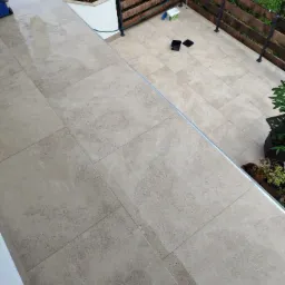 Beżowe płytki gresowe na balkonie po umyciu, widoczna drewniana balustrada i rośliny w donicach.