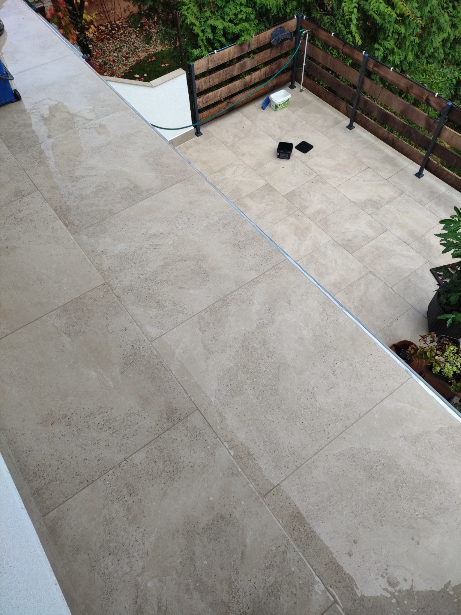 Beżowe płytki gresowe na balkonie po umyciu, widoczna drewniana balustrada i rośliny w donicach.