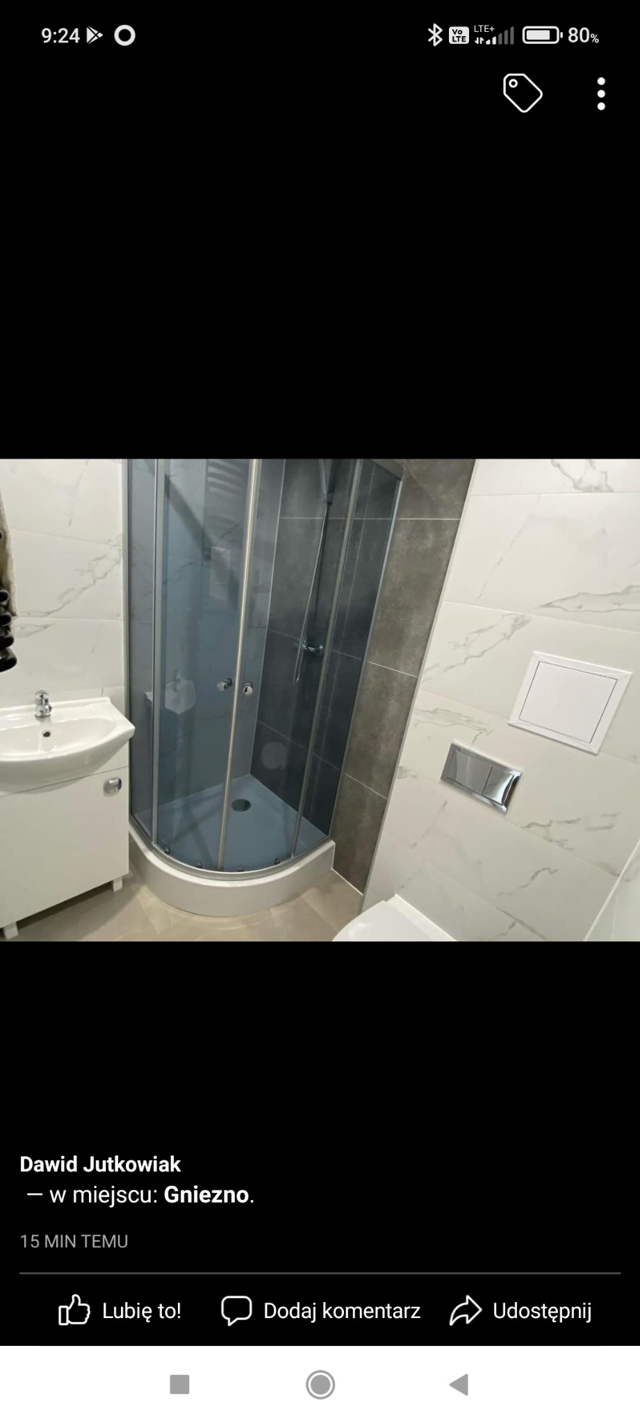 Nowoczesna łazienka po remoncie: narożna kabina prysznicowa z szarymi płytkami, biała umywalka z szafką, toaleta i białe marmurowe płytki na ścianach, widoczne chromowane elementy.