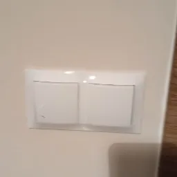 Biały, podwójny włącznik światła zamontowany na kremowej ścianie.