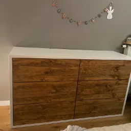 Komoda z sześcioma szufladami z ciemnego drewna, biały blat i obramowanie, dekoracja świąteczna na ścianie, widok z bliska.