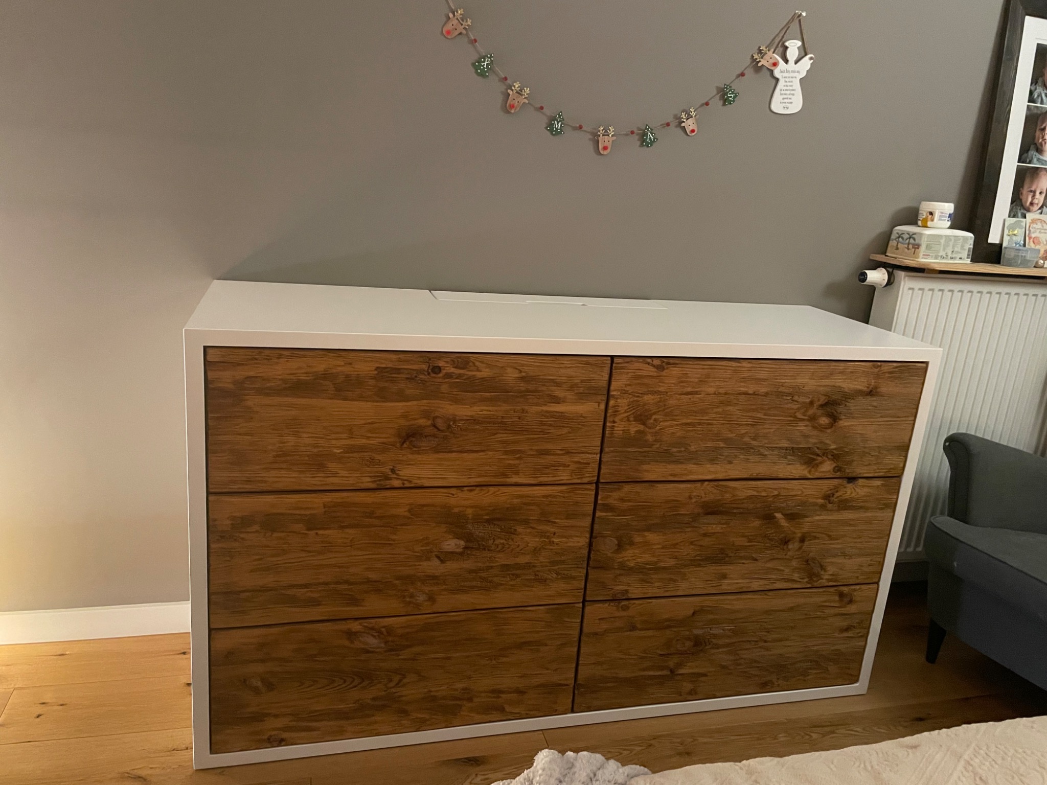 Komoda z sześcioma szufladami z ciemnego drewna, biały blat i obramowanie, dekoracja świąteczna na ścianie, widok z bliska.