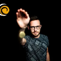 Hipnoterapeuta w okularach, z brodą, ubrany w koszulkę we wzory, trzymający wahadełko na czarnym tle, z logo firmy w lewym górnym rogu.