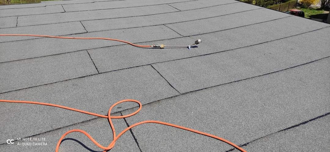 Szary dach pokryty papą termozgrzewalną z widocznym kablem zasilającym narzędzie dekarskie.