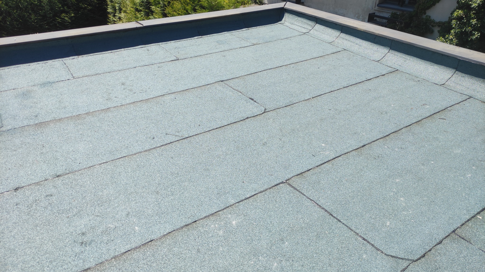 Pokrycie dachu papą termozgrzewalną w odcieniach szarości i zieleni, widoczne łączenia i obróbki blacharskie przy krawędzi dachu.