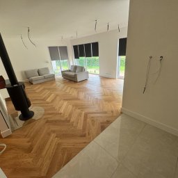 KOZ-BUD - Salon po remoncie z parkietem w jodełkę, kominkiem i wyprowadzonymi kablami w ścianie. Jasne wnętrze, nowoczesny design.