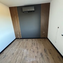 KOZ-BUD - Nowoczesne wnętrze z drewnianymi lamelami na ścianie, szarą farbą i klimatyzacją. Jasna podłoga z paneli, widoczne gniazdka elektryczne.