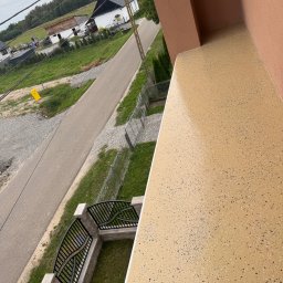 KOZ-BUD - Balkon z beżową, żywiczną posadzką z ciemnymi drobinkami, widok z góry na ogrodzenie i ulicę. Nowoczesne wykończenie balkonu.