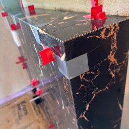 KOZ-BUD - Montaż ciemnych płytek imitujących marmur z użyciem poziomujących klipsów i taśmy. Widoczny fragment pomieszczenia w trakcie prac wykończeniowych.