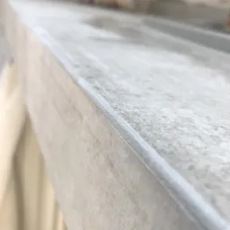 Detal na krawędzi ściany po nałożeniu gładzi, widoczna faktura materiału i osoba w tle w rozmyciu.