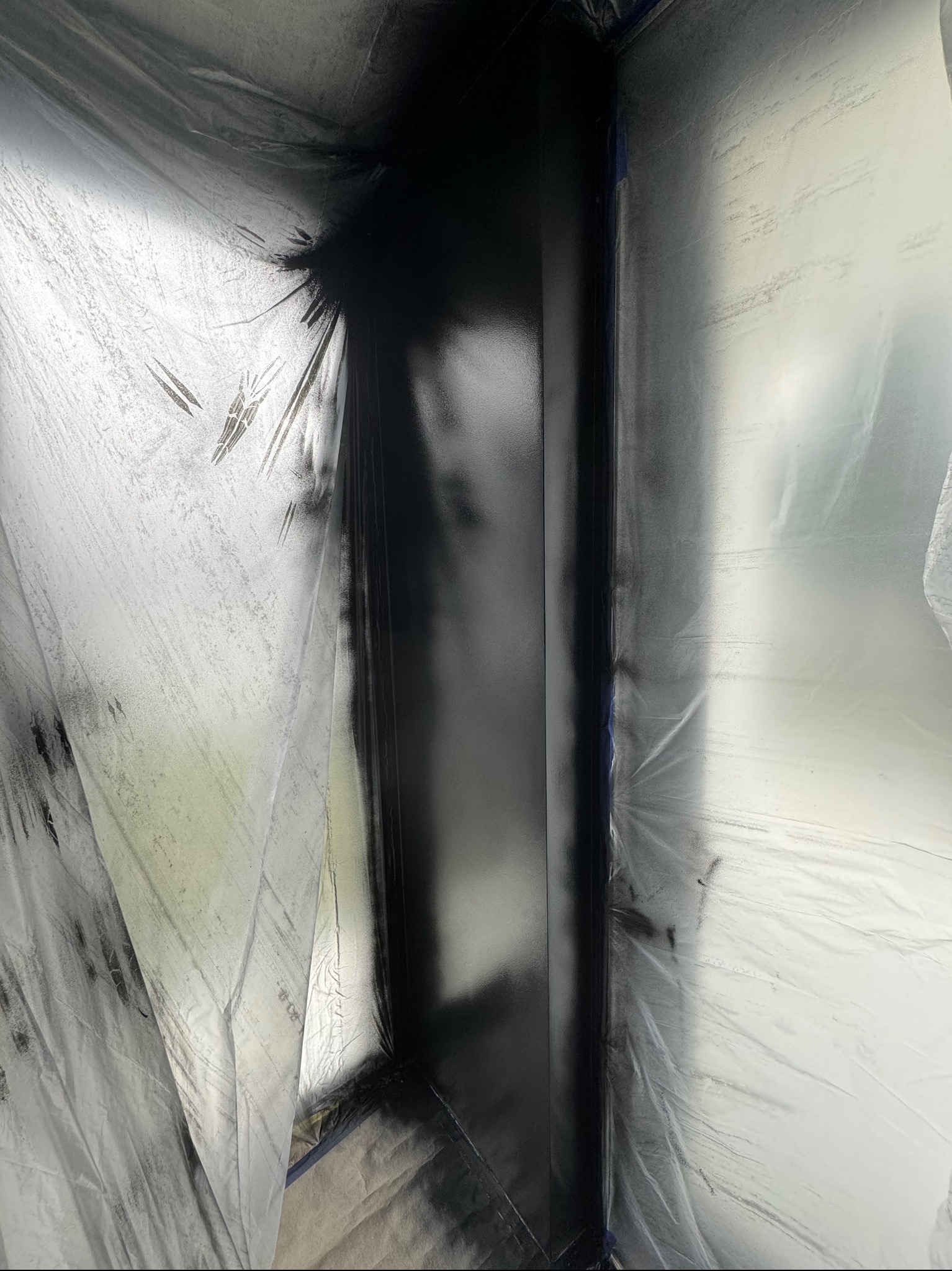 Świeżo pomalowany na czarno fragment ściany zabezpieczony folią malarską, widoczne ślady farby na folii.