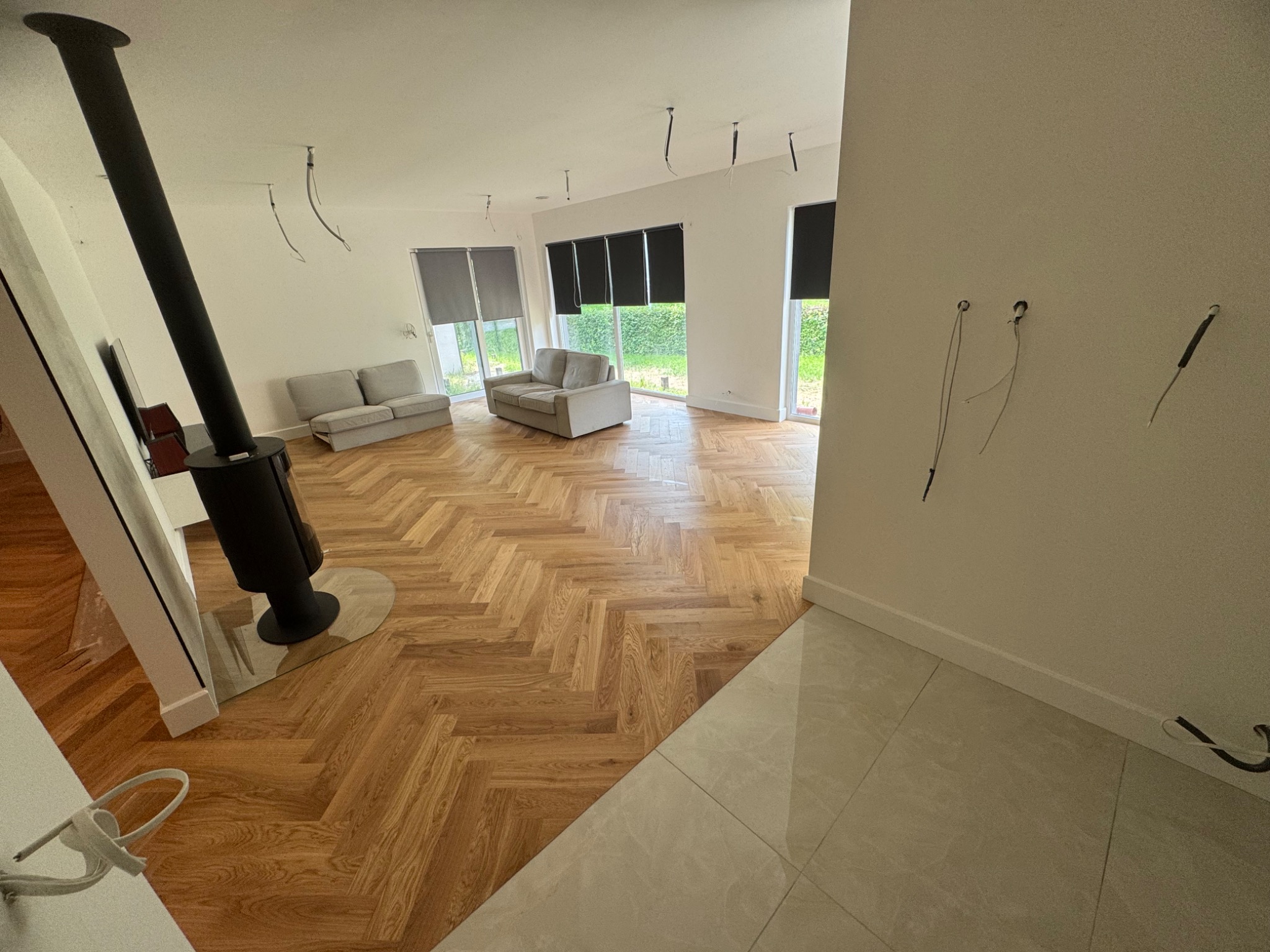 Salon po remoncie z parkietem w jodełkę, kominkiem i wyprowadzonymi kablami w ścianie. Jasne wnętrze, nowoczesny design.