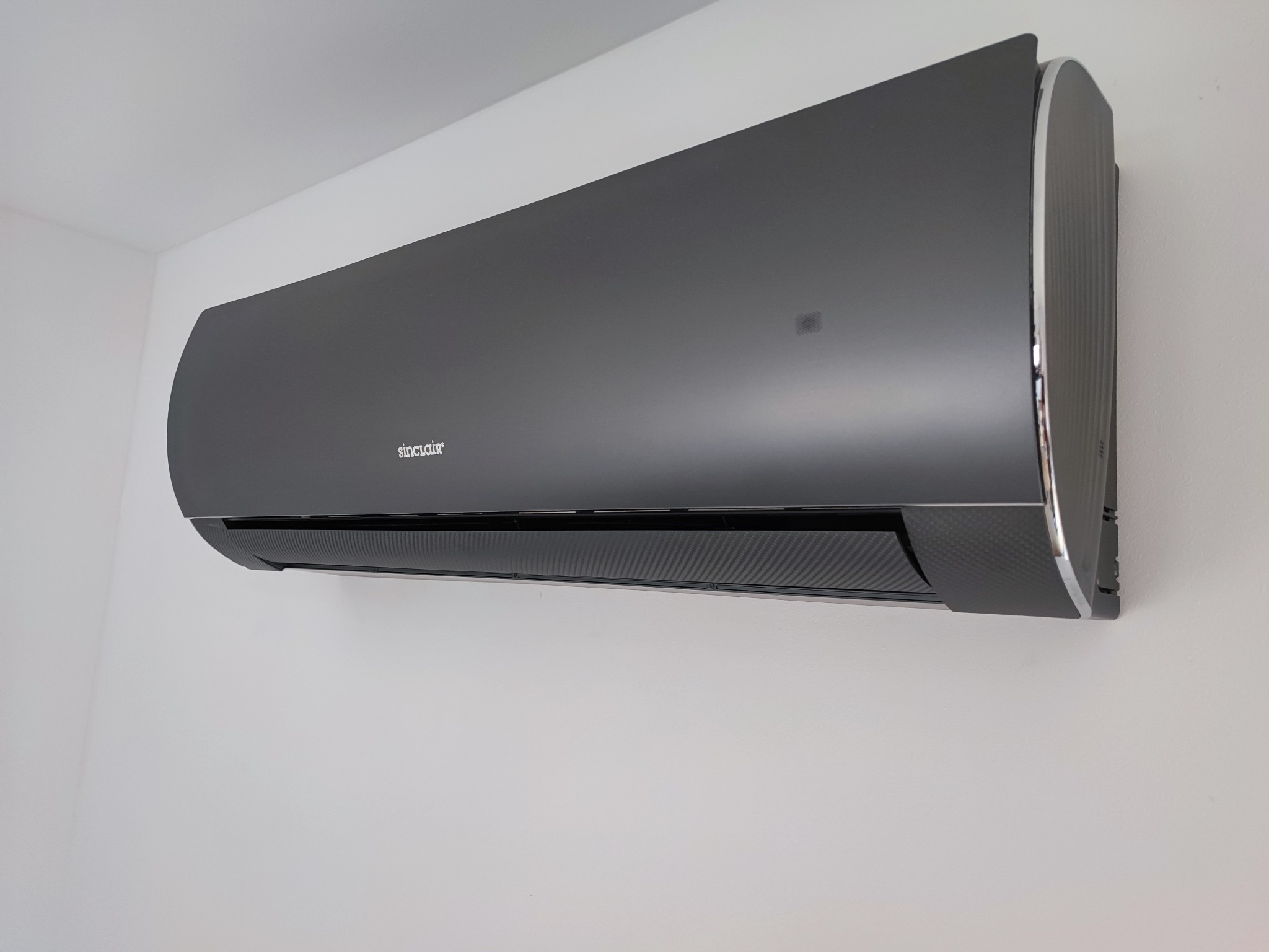 Nowoczesny, grafitowy klimatyzator Sinclair zamontowany na białej ścianie, widoczny z boku z delikatnym połyskiem.