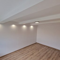 ODNOWA-Uslugi Remontowe Ihor Chornyi - Pusty pokój po remoncie z panelami podłogowymi, białymi ścianami, listwami przypodłogowymi, sufitem z belkami i oświetleniem punktowym.