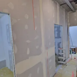 Montaż płyt kartonowo-gipsowych na metalowym stelażu, widoczne pionowe linie wyznaczające punkty mocowania, fragment instalacji elektrycznej pod sufitem.