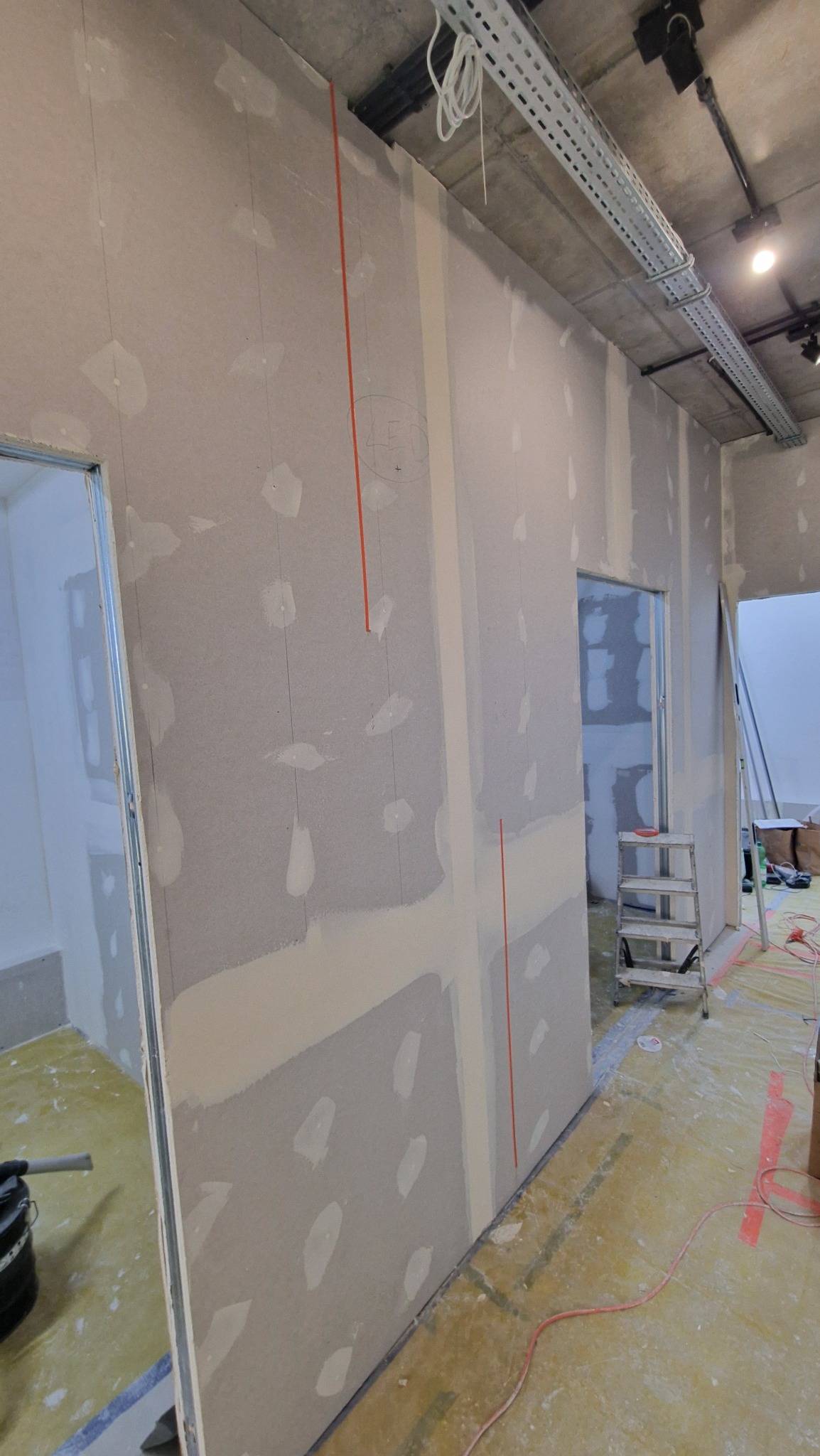 Montaż płyt kartonowo-gipsowych na metalowym stelażu, widoczne pionowe linie wyznaczające punkty mocowania, fragment instalacji elektrycznej pod sufitem.
