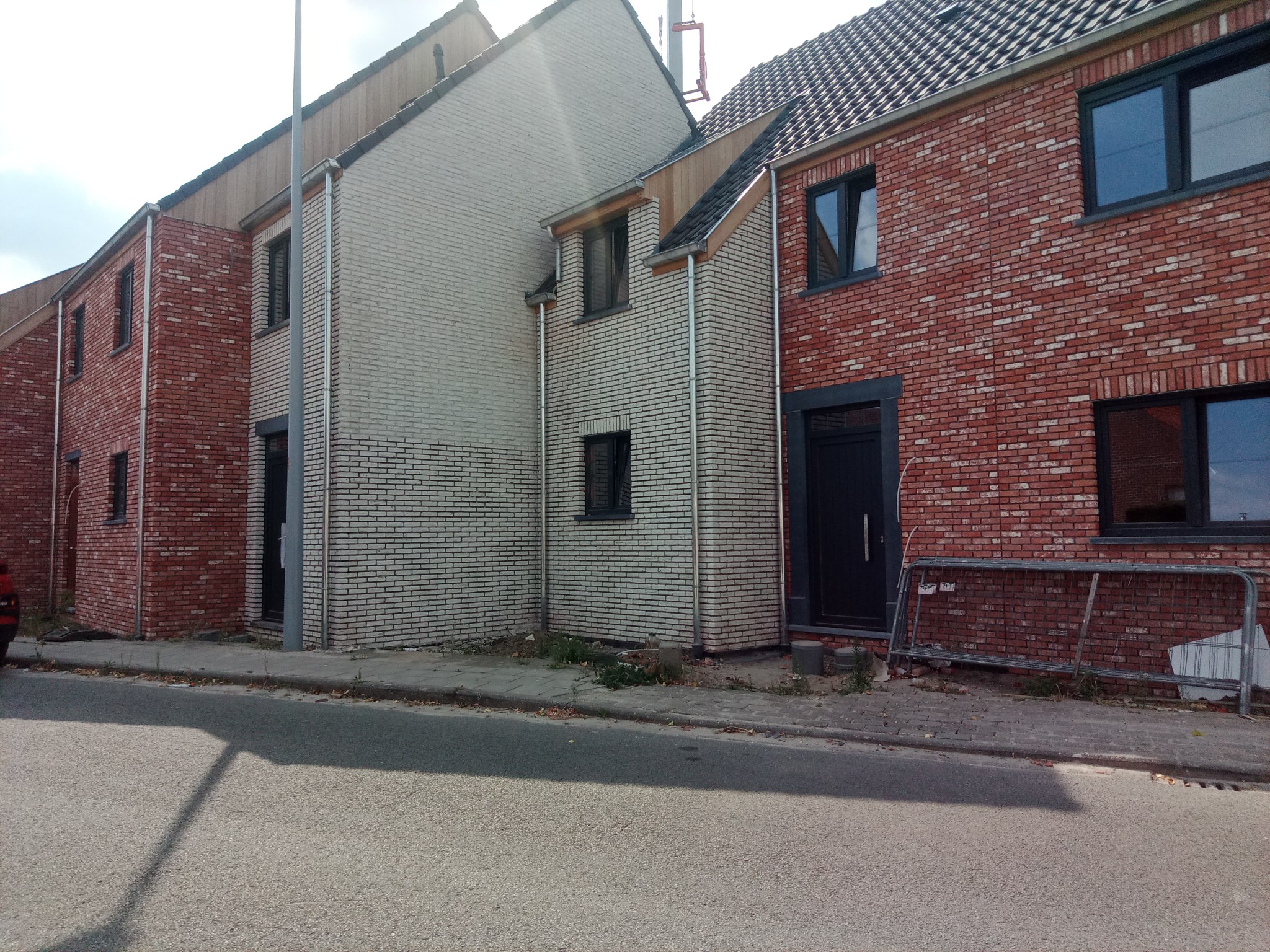 Nowe budynki mieszkalne z czerwonej i białej cegły, z widocznymi rynnami i elementami wykończeniowymi dachu, częściowo zasłonięte przez cień słupa.