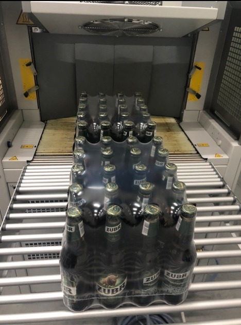 Zgrzewka piwa Żubr, owinięta folią termokurczliwą, na linii produkcyjnej z rolkami.