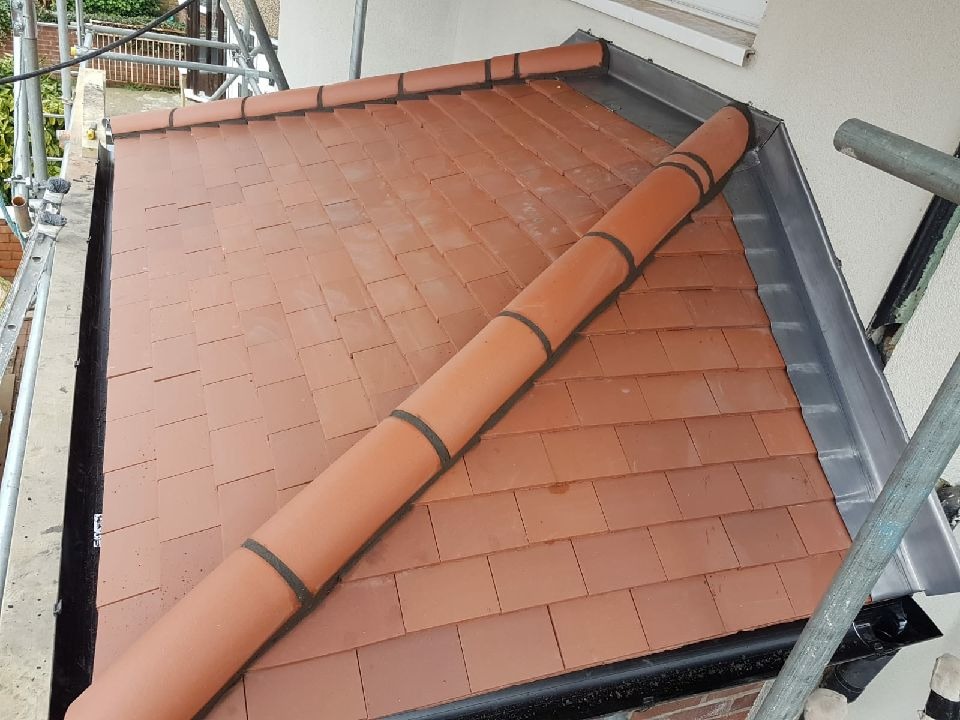 Nowo ułożona dachówka ceramiczna w kolorze ceglastym, widoczne obróbki blacharskie i element systemu rynnowego, ujęcie z rusztowania.