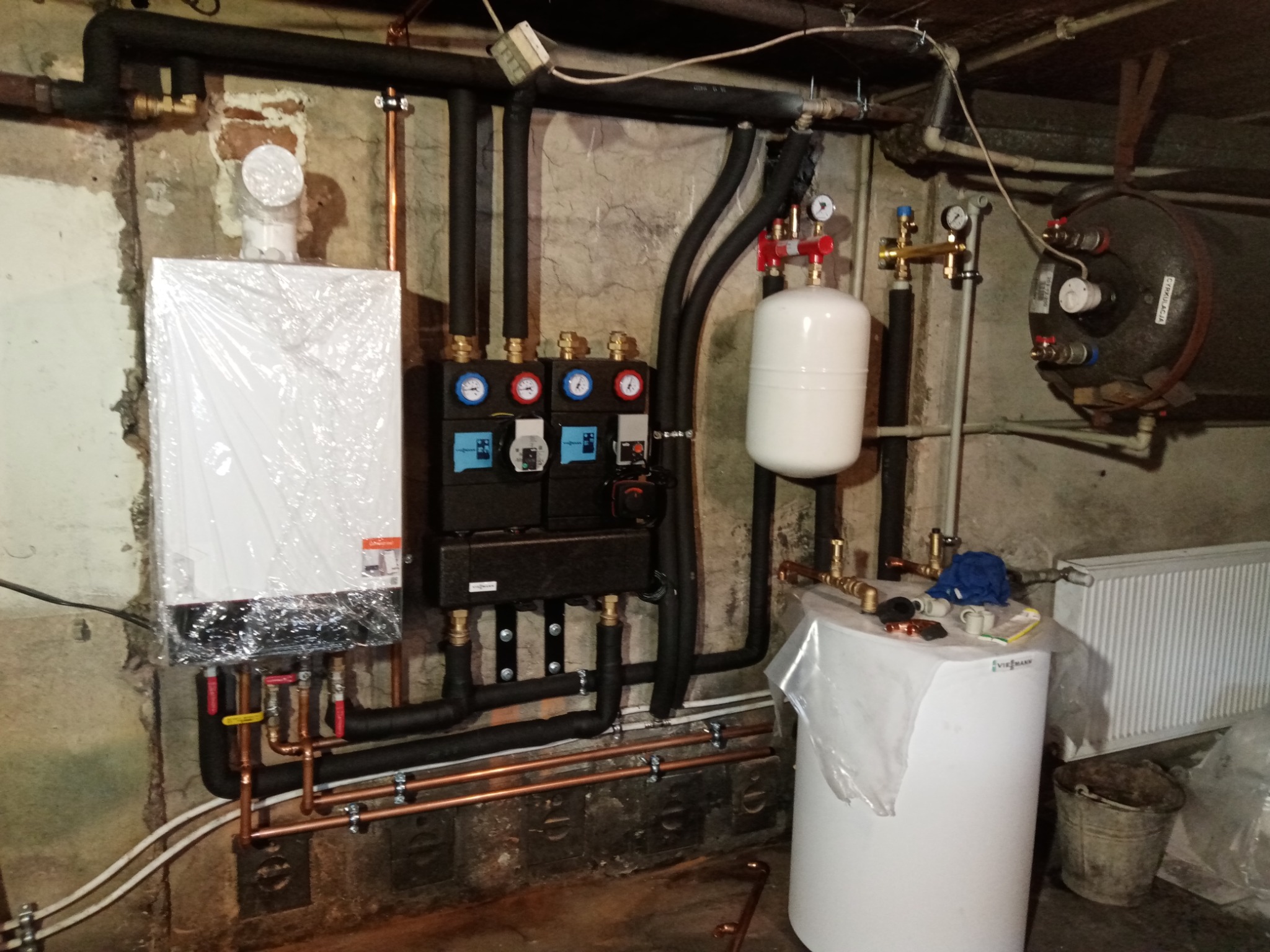 Nowy, jeszcze ofoliowany piec grzewczy Viessmann zamontowany w piwnicy, z widocznymi rurami miedzianymi i czarnymi izolowanymi, podłączony do zbiornika wyrównawczego i zasobnika ciepłej wody,...