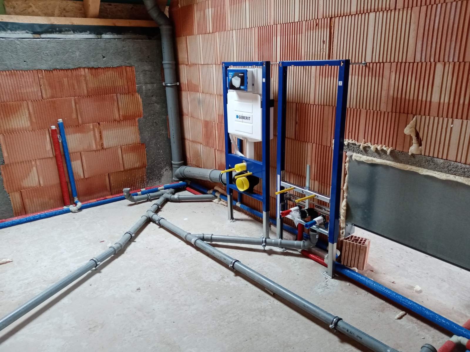 Stelaż podtynkowy Geberit Duofix z widocznymi rurami kanalizacyjnymi i wodnymi w surowym stanie, ściana z cegły kratówki.