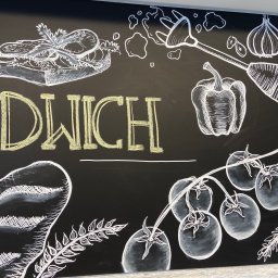ELERTs DESIGN - Tablica kredowa z rysunkiem kanapki, warzyw i napisem 'SANDWICH' wykonanym żółtą kredą, stylizowana na menu restauracji.