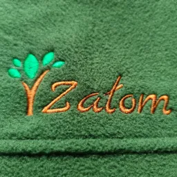 Zielony polar z wyhaftowanym pomarańczowym napisem 'Zatom' i stylizowanym drzewkiem z zielonymi listkami.