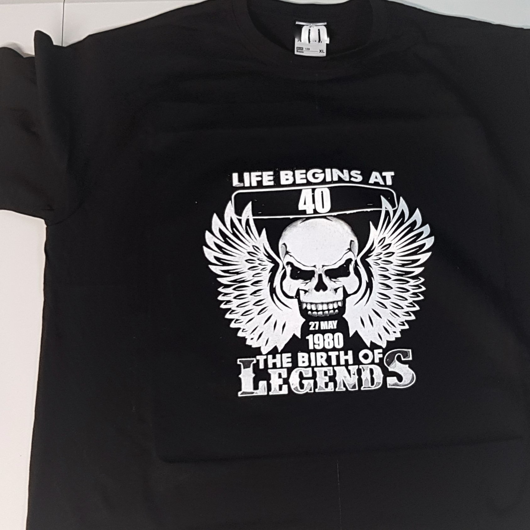 Czarna koszulka z białym nadrukiem czaszki ze skrzydłami i napisem 'Life begins at 40' oraz '27 May 1980 The Birth of Legends'.