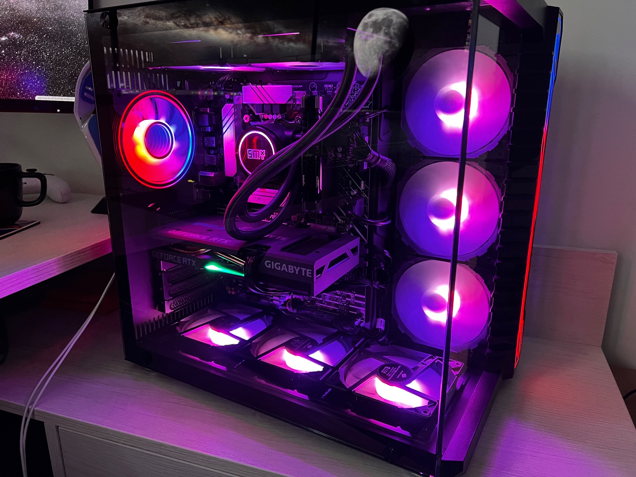 Przezroczysta obudowa komputera stacjonarnego z podświetleniem RGB na wentylatorach, chłodzeniu cieczą procesora i karcie graficznej GeForce RTX, widoczna na biurku.