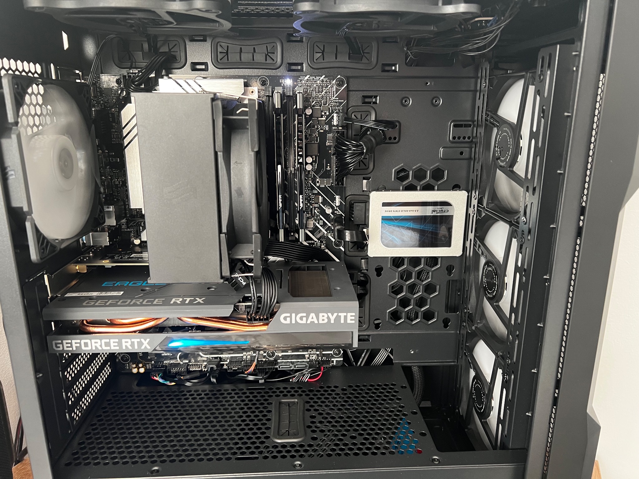 Wnętrze obudowy komputera stacjonarnego z kartą graficzną Gigabyte GeForce RTX, chłodzeniem procesora, dyskiem SSD Crucial i wentylatorami z białymi łopatkami.