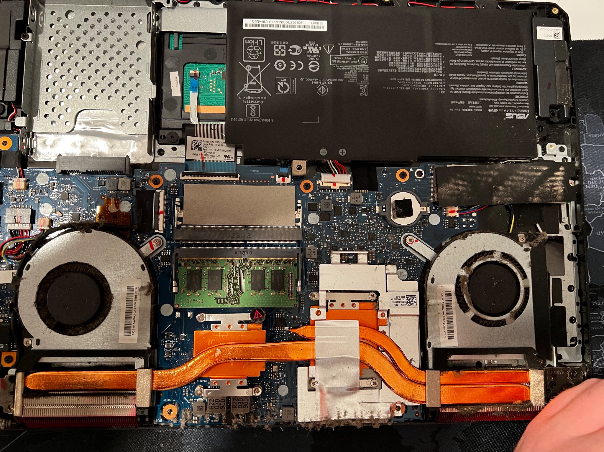 Wnętrze otwartego laptopa ASUS z widoczną baterią, wentylatorami i płytą główną, pokryte kurzem i zabrudzeniami.