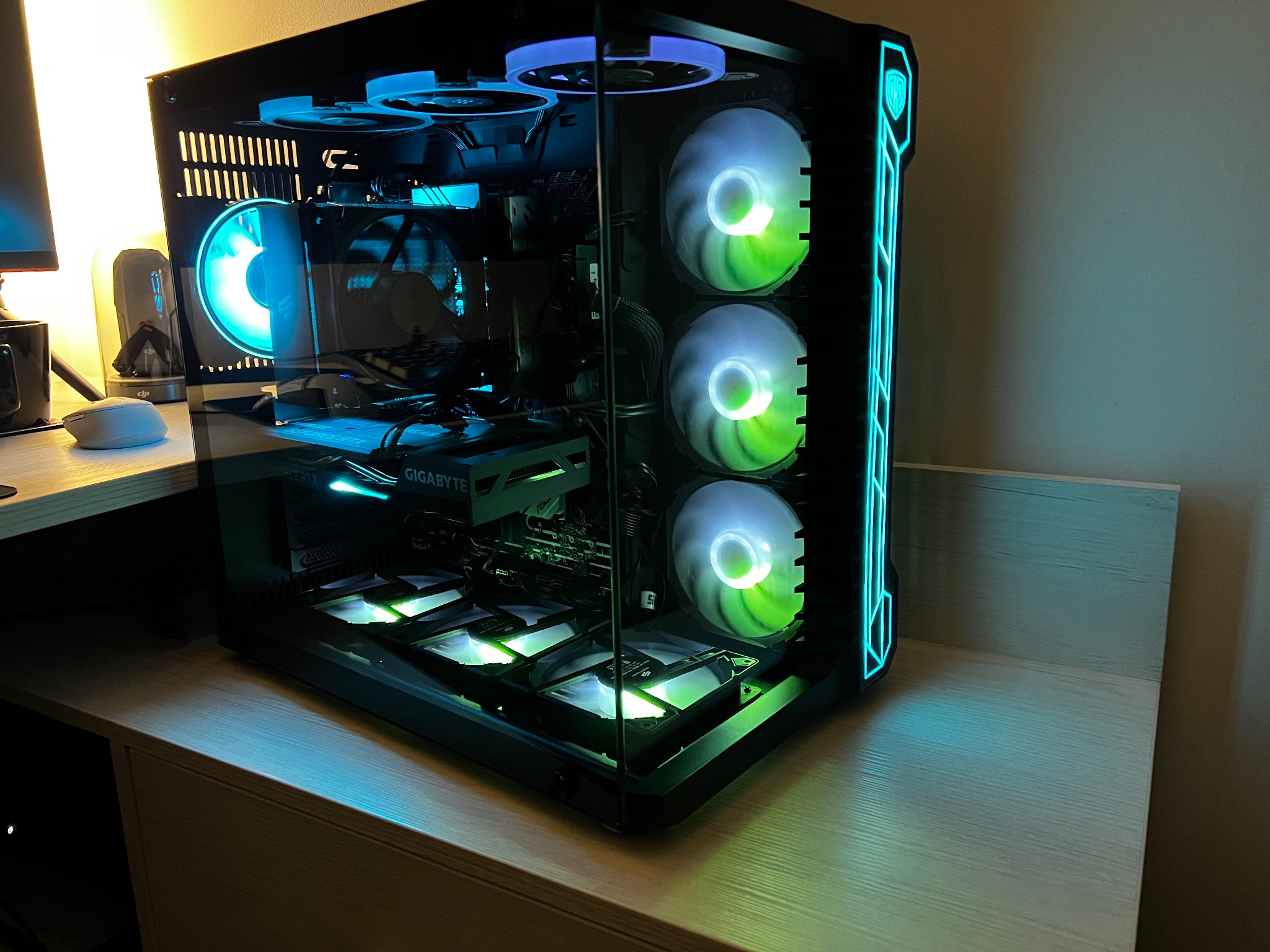 Przezroczysta obudowa komputera stacjonarnego z podświetleniem RGB na wentylatorach, płycie głównej i karcie graficznej Gigabyte, stojąca na jasnym biurku.
