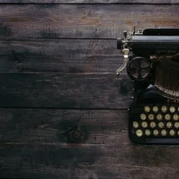 Czarna, zabytkowa maszyna do pisania Corona na tle ciemnych, drewnianych desek, widok z góry, oświetlenie naturalne.