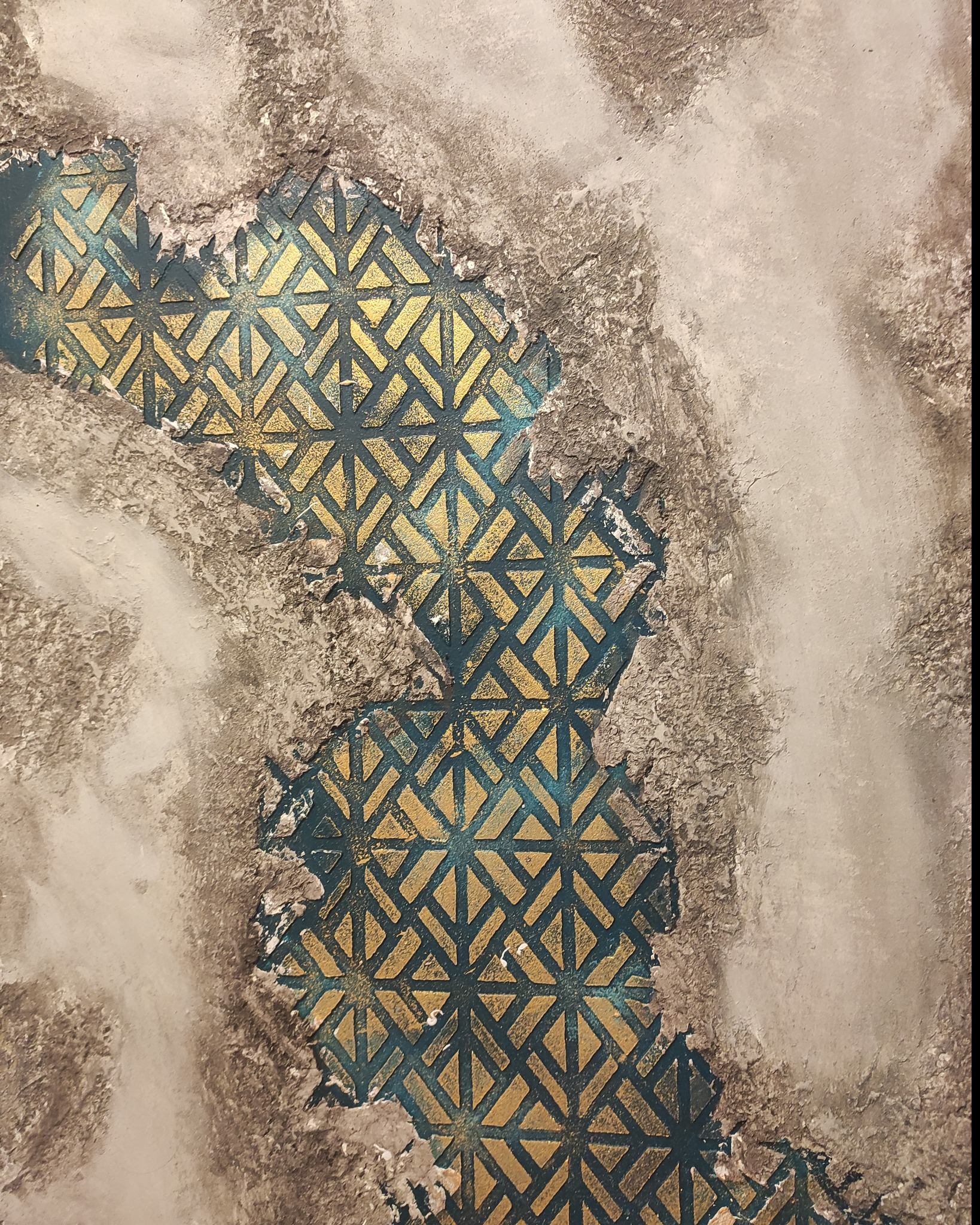 Fragment dekoracyjnej ściany z wzorem geometrycznym w kolorach złota i turkusu, częściowo pokrytej szarą, strukturalną farbą imitującą surowy beton.