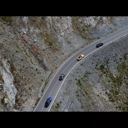 Spotlight Films Jakub Kiełtucki - Panoramiczne ujęcie z drona na krętą drogę górską z jadącymi samochodami w różnych kolorach: niebieskim, szarym, żółtym i czarnym. Skaliste zbocza po obu stronach drogi.
