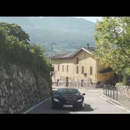 Spotlight Films Jakub Kiełtucki - Czarny Lamborghini Huracan na drodze w malowniczej scenerii górskiej, z budynkiem w tle i przechodzącą kobietą. Ujęcie z niskiej perspektywy.