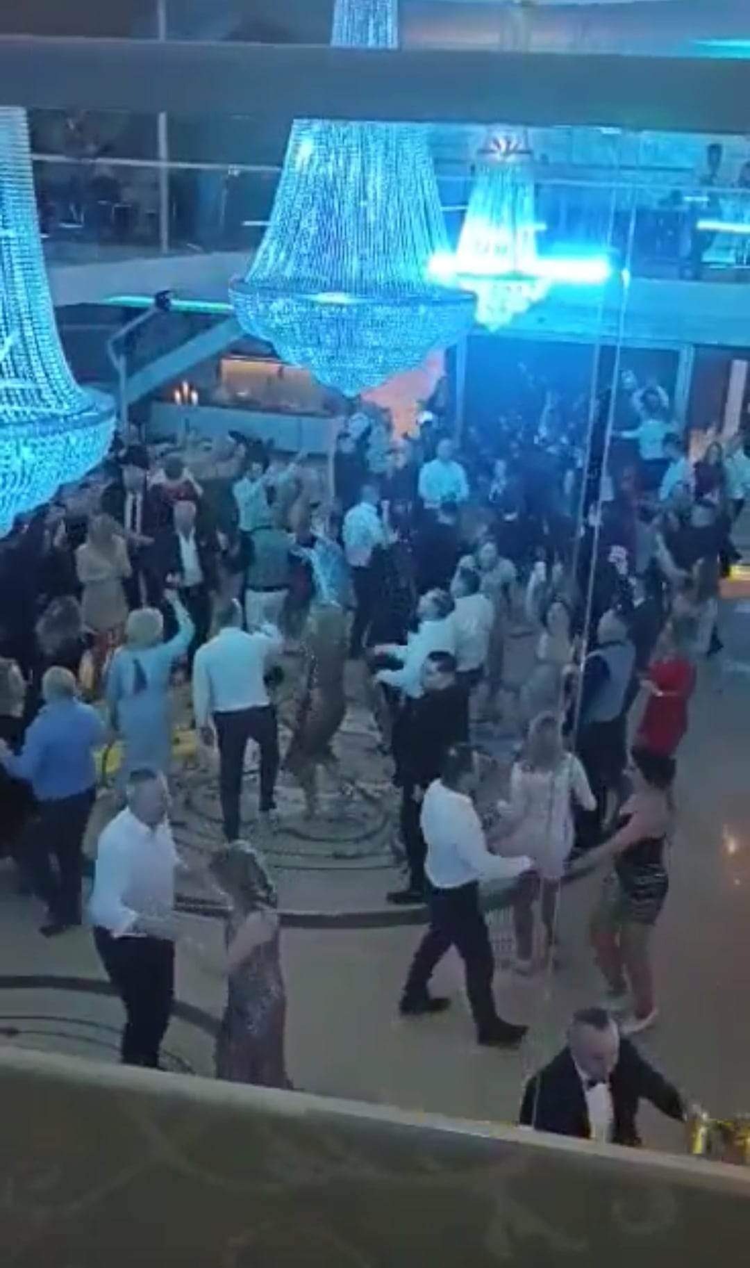 Sala balowa z parkietem wypełnionym tańczącymi gośćmi, oświetlona kaskadowymi żyrandolami w odcieniach błękitu.