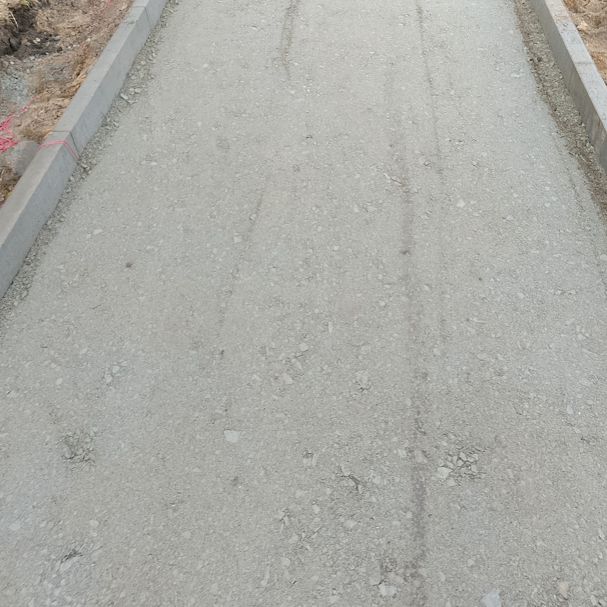 Podbudowa drogi z obrzeżami betonowymi, widok z góry. Przygotowanie podłoża pod nawierzchnię, etap prac ziemnych.