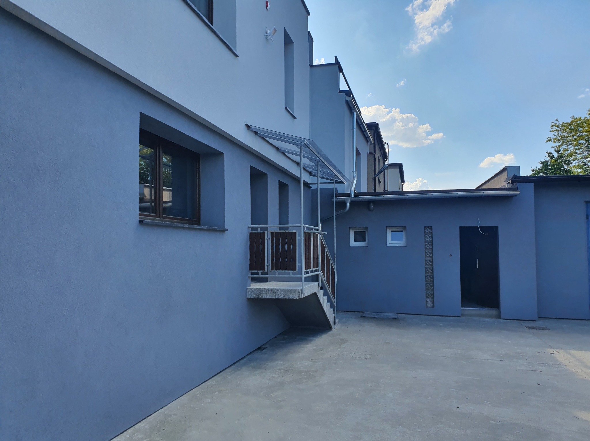 Budynek po renowacji elewacji w Tarnowskich Górach, z widocznym wejściem z zadaszeniem i świeżo pomalowaną fasadą w odcieniach szarości.