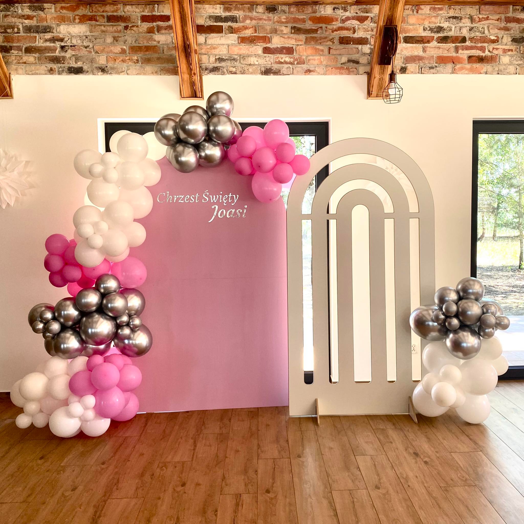 Dekoracja na Chrzest Święty Joasi, z różowym tłem, białymi, różowymi i srebrnymi balonami oraz drewnianym parawanem w kształcie łuku.