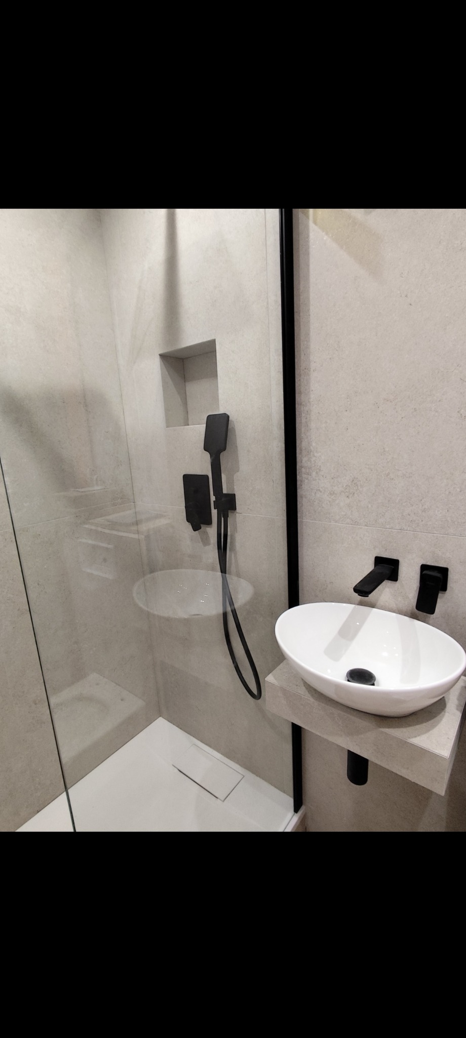 Nowoczesna łazienka z kabiną prysznicową typu walk-in i umywalką nablatową. Czarna armatura, beżowe płytki. Minimalistyczny design z akcentem na funkcjonalność.