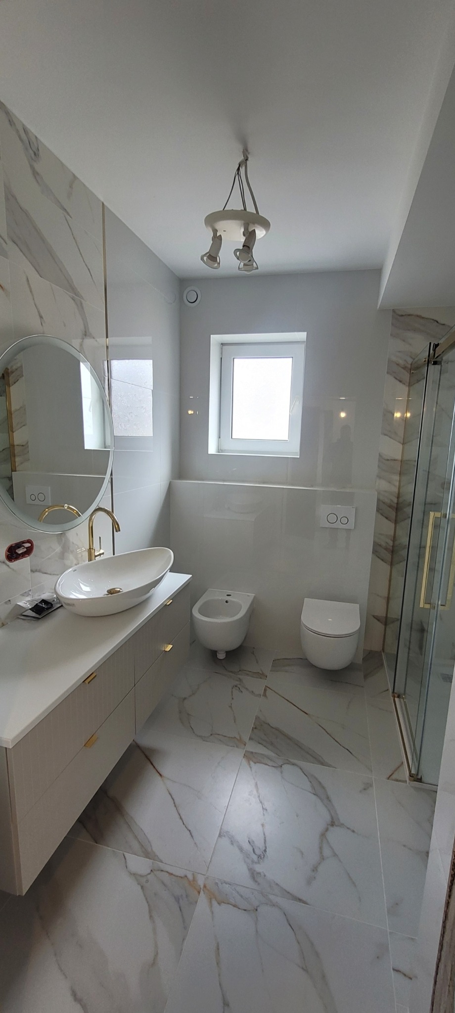 Elegancka łazienka w bieli i marmurze: owalne umywalki, złote akcenty, kabina prysznicowa i nowoczesne oświetlenie. Wykończenie wnętrz z dbałością o detale.