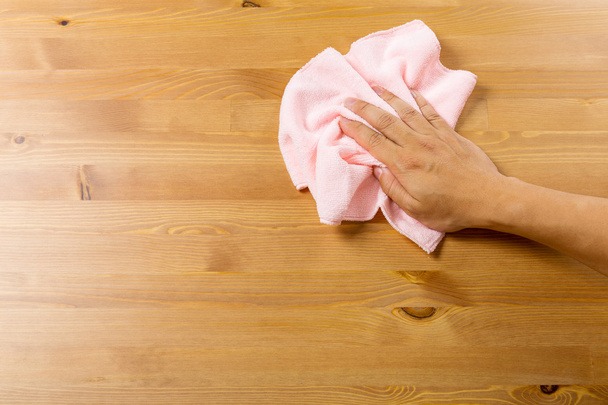 Ręka przeciera różową ściereczką drewniany blat stołu w Łomży, widoczne słoje drewna.