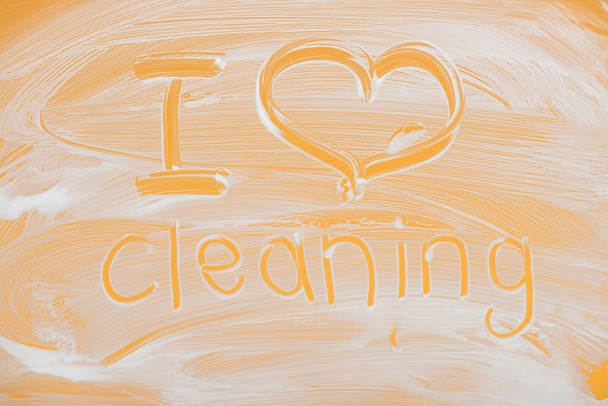 Napis 'I love cleaning' wykonany z piany na pomarańczowej powierzchni.